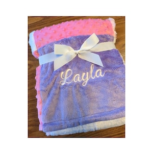 May include: A purple and pink baby blanket with a white satin ribbon and bow. The blanket is personalized with the name "Layla" embroidered in white.