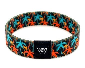 May include: A black woven bracelet with a colorful palm tree pattern and a black adjustable buckle with a white "shaka" hand gesture.