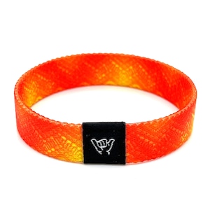 May include: Orange and yellow woven wristband with a black adjustable clasp. The clasp has a white "shaka" hand symbol.