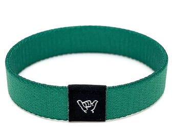 May include: A green woven wristband with a black label featuring a white "shaka" hand gesture.