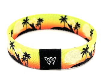 May include: A yellow, orange, and white woven bracelet with a black silhouette of palm trees and a sunset. The bracelet has a black adjustable clasp with a white "shaka" hand symbol.