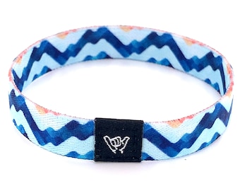 May include: A blue and white patterned wristband with a black adjustable buckle. The buckle has a white "shaka" hand symbol.
