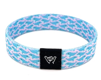May include: A blue and pink patterned woven bracelet with a black adjustable buckle featuring a white "shaka" hand gesture.