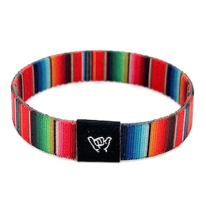 May include: A colorful woven bracelet with a black adjustable buckle featuring a white "shaka" hand gesture.