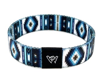 Puede incluir: Una pulsera tejida de color azul y blanco con un cierre ajustable negro que presenta un gesto de mano "shaka" blanco.