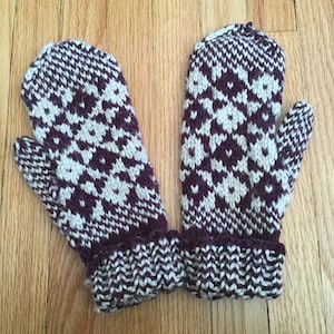 以下が含まれることがあります： 白とワインレッドの幾何学模様のニットミトン。ミトンはリブ編みのカフス付きです。