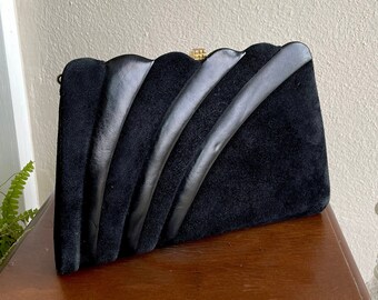 May include: A black suede clutch bag with a decorative design of overlapping black leather strips. The bag has a gold-toned clasp.
