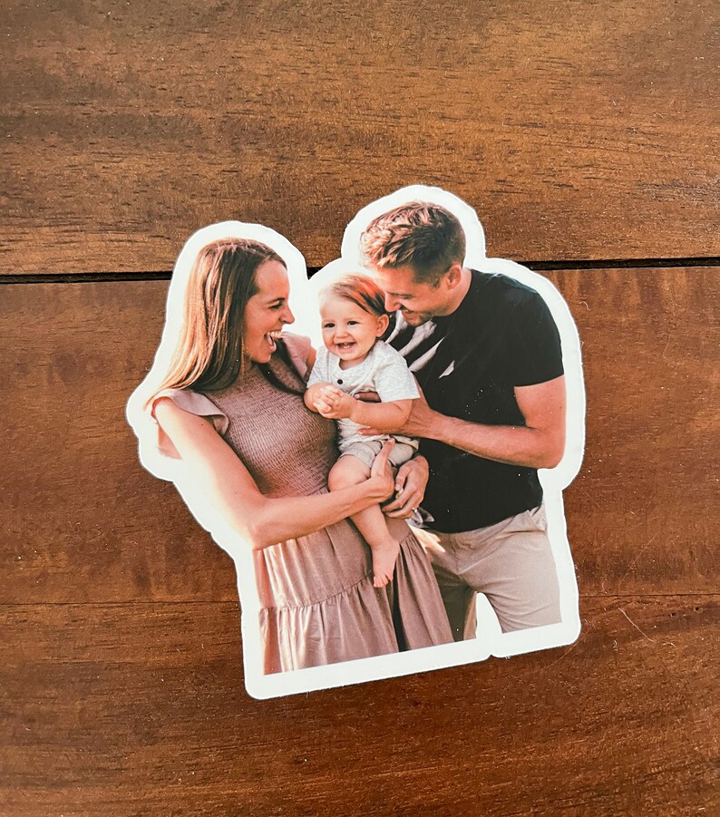 May include: A family portrait of a couple holding their baby. The parents are smiling and looking at the baby, who is laughing. The baby is wearing a white shirt and the parents are wearing casual clothing.