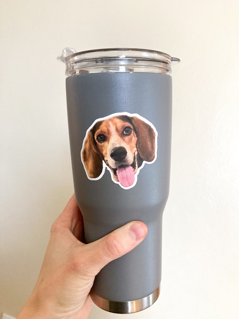 May include: A gray stainless steel travel mug with a sticker of a beagle dog with brown and white fur and a pink tongue sticking out.