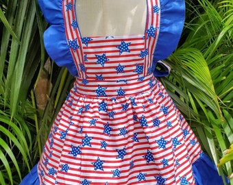 May include: A blue and red dress with a white star pattern. The dress has a ruffled neckline and a ruffled hem. The dress is paired with a matching headband.