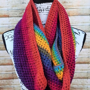 May include: A colorful crocheted infinity scarf with stripes of purple, red, orange, blue, green, and yellow.
