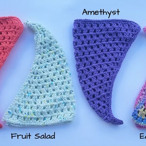 May include: Four crocheted triangle hats in different colors: coral, light blue with white flecks, purple, and a rainbow pattern. The hats are labeled "Coral", "Fruit Salad", "Amethyst", and "Eastern Nova".