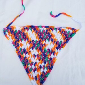 May include: A colorful crocheted triangle scarf with white, orange, green, blue, and pink yarn. The scarf has long ties that can be tied around the neck.