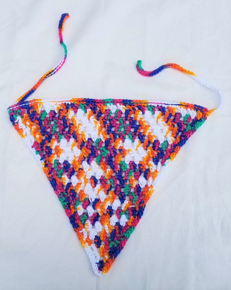 May include: A colorful crocheted triangle scarf with white, orange, green, blue, and pink yarn. The scarf has long ties that can be tied around the neck.