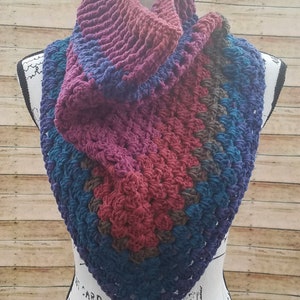 May include: A crocheted cowl in shades of purple, blue, and brown. The cowl is folded and draped over a white mannequin.