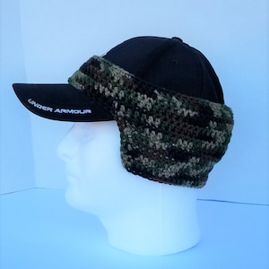 May include: A black baseball cap with a camouflage crochet ear warmer attached. The cap has the words "Under Armour" embroidered on the brim.