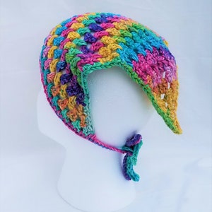 May include: A colorful crocheted baby bonnet with a tie. The bonnet is made with a variety of colors, including pink, blue, green, yellow, and purple.
