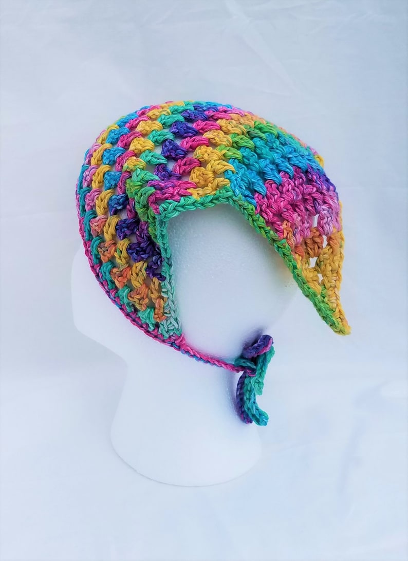 May include: A colorful crocheted baby bonnet with a tie. The bonnet is made with a variety of colors, including pink, blue, green, yellow, and purple.