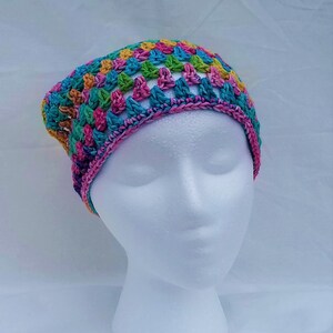 May include: A colorful crocheted hat with a rainbow pattern. The hat is made with a variety of colors, including pink, blue, green, yellow, and orange.