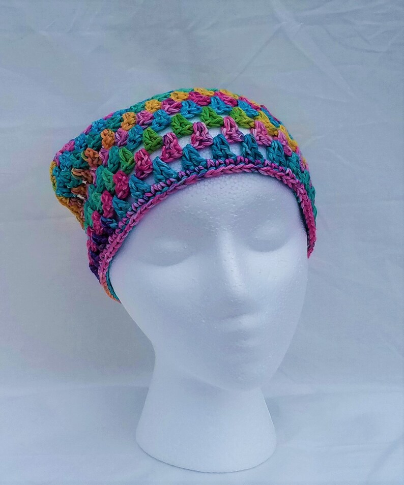 May include: A colorful crocheted hat with a rainbow pattern. The hat is made with a variety of colors, including pink, blue, green, yellow, and orange.