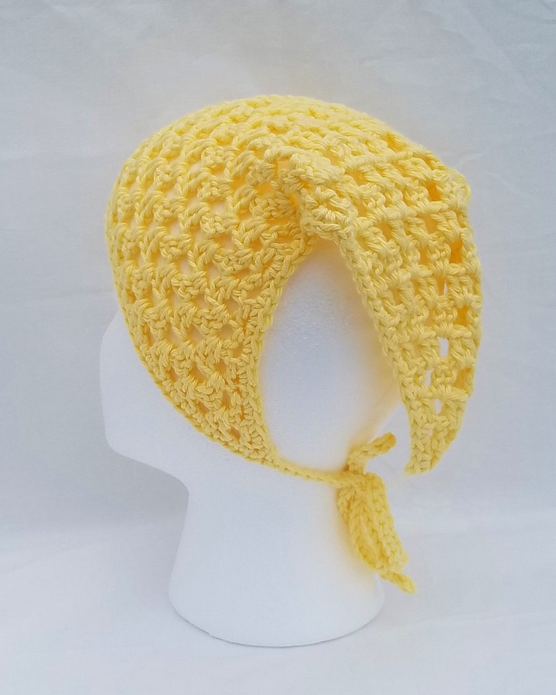 May include: A yellow crocheted hat with a tie at the back. The hat is made with a simple stitch pattern and has a loose, airy feel.