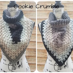 May include: Two crocheted cowl neck scarves, one in black, gray, and beige, and the other in gray, beige, and blue. The scarves are displayed on a mannequin with the text "Cookie Crumble" above them.