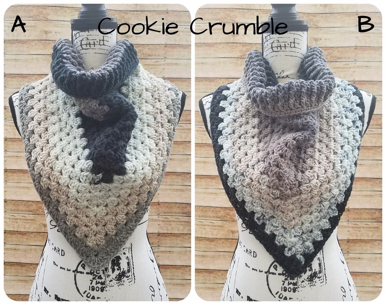 May include: Two crocheted cowl neck scarves, one in black, gray, and beige, and the other in gray, beige, and blue. The scarves are displayed on a mannequin with the text "Cookie Crumble" above them.