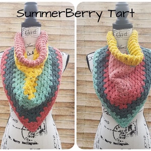 May include: Two crocheted infinity scarves, one in shades of teal, yellow, and pink, and the other in shades of pink, teal, and gray. The scarves are displayed on a white mannequin with a wooden base. The text "Summer Berry Tart" is written above the scarves.