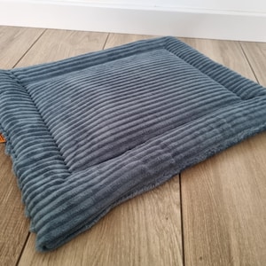Puede incluir: Una cama rectangular para mascotas de pana azul con una textura suave y acanalada. La cama tiene un borde elevado. El color suave y el diseño sencillo lo convierten en un complemento acogedor para cualquier hogar.
