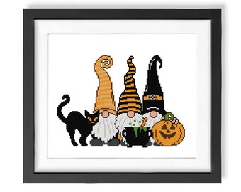 Op de afbeelding: Drie gnomen gekleed in oranje en zwarte Halloween-kostuums met een zwarte kat en een jack-o'-lantern. De gnomen houden een ketel met groene vloeistof.