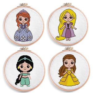 Puede incluir: Cuatro aros de bordado de punto de cruz con personajes de princesas de dibujos animados. Cada princesa viste un vestido colorido y tiene cabello y accesorios únicos. Los aros son redondos con un marco de madera y tela blanca.