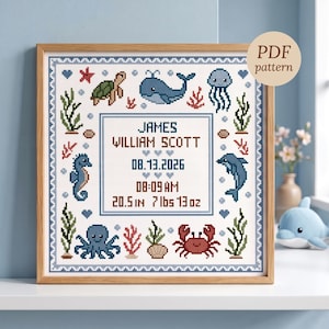 May include: A framed cross-stitch birth announcement featuring sea creatures including a turtle, whale, jellyfish, seahorse, dolphin, octopus, and crab. The text reads JAMES WILLIAM SCOTT, 08.13.2026, 08:09 AM, 20.5 in, 7 lbs 13 oz, with a PDF pattern label.