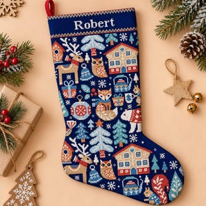 Peut inclure: Une chaussette de Noël bleu foncé avec un motif au point de croix représentant des maisons, des rennes, des hiboux, des renards, des écureuils et des arbres. Le prénom Robert est brodé en blanc en haut. Elle possède une boucle de suspension rouge.