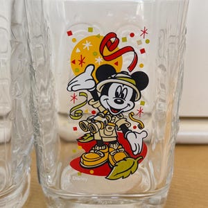 以下が含まれることがあります： サファリ衣装のミッキーマウスが双眼鏡を持っているカラフルなグラフィックが特徴の透明なガラス。デザインには、黄色の太陽、赤いリボン、紙吹雪が含まれています。ガラスの底には「2000」とディズニーのロゴが刻印されています。
