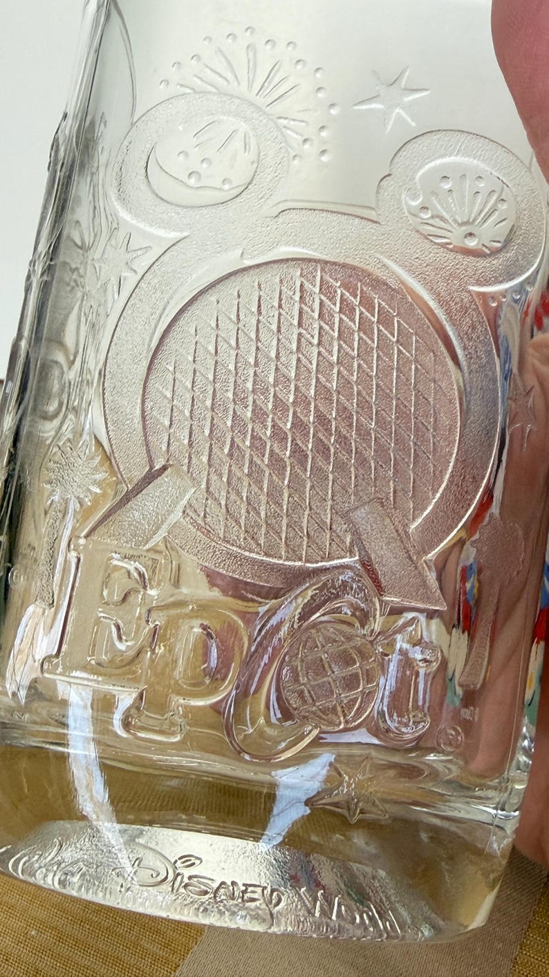 以下が含まれることがあります： 「Epcot」の文字と地球儀がエンボス加工された透明なガラスタンブラー。ミッキーマウスの頭やその他の装飾要素も付いています。「Disney World」の文字が下部にあります。