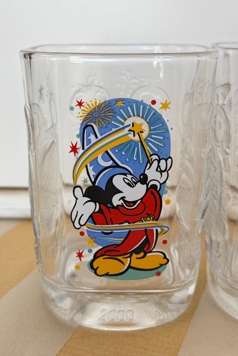 以下が含まれることがあります： ミッキーマウスが魔法使いの衣装を着て、星の杖を持っているカラフルなグラフィックが特徴の透明なガラス。 デザインには花火と2000年が含まれています。 ガラスには装飾的なエンボス加工が施されています。
