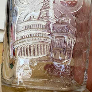 以下が含まれることがあります： ドーム型の建物や塔など、エンボス加工された建築デザインが施された透明なガラスタンブラー。「Disney World」の文字が底にあり、お土産品である可能性が高いです。