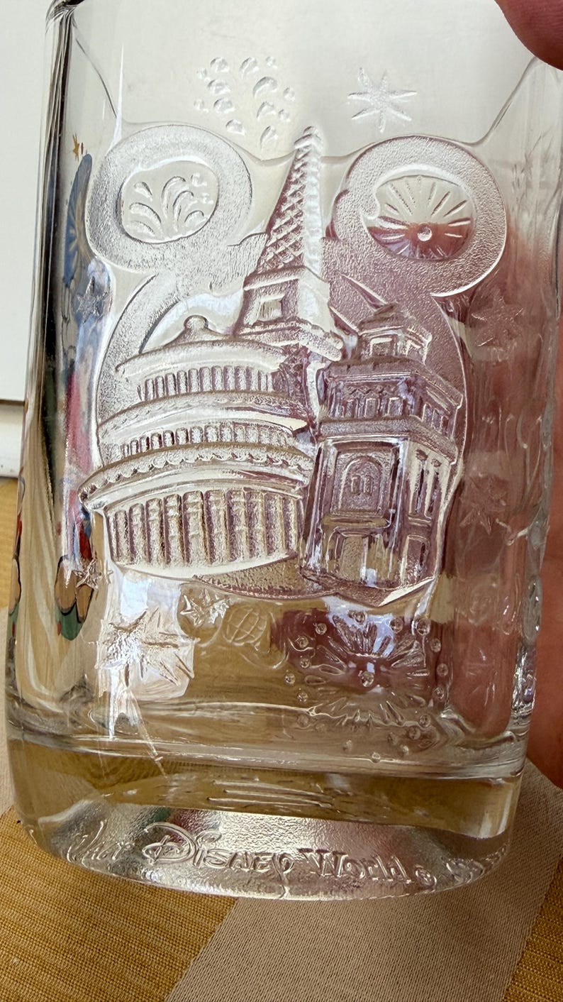 以下が含まれることがあります： ドーム型の建物や塔など、エンボス加工された建築デザインが施された透明なガラスタンブラー。「Disney World」の文字が底にあり、お土産品である可能性が高いです。