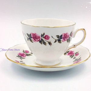 May include: A white teacup and saucer with a gold rim and a pink rose floral pattern.