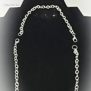 May include: A silver chain necklace with a lobster clasp closure. The chain is on a black background.