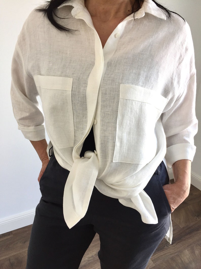 May include: A white linen shirt with long sleeves and two large pockets. The shirt is tied at the waist.