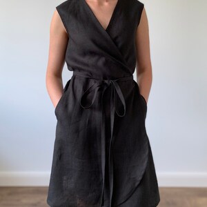 May include: A black linen wrap dress with a V-neckline and a tie belt. The dress has pockets on the sides and a slightly flared skirt.