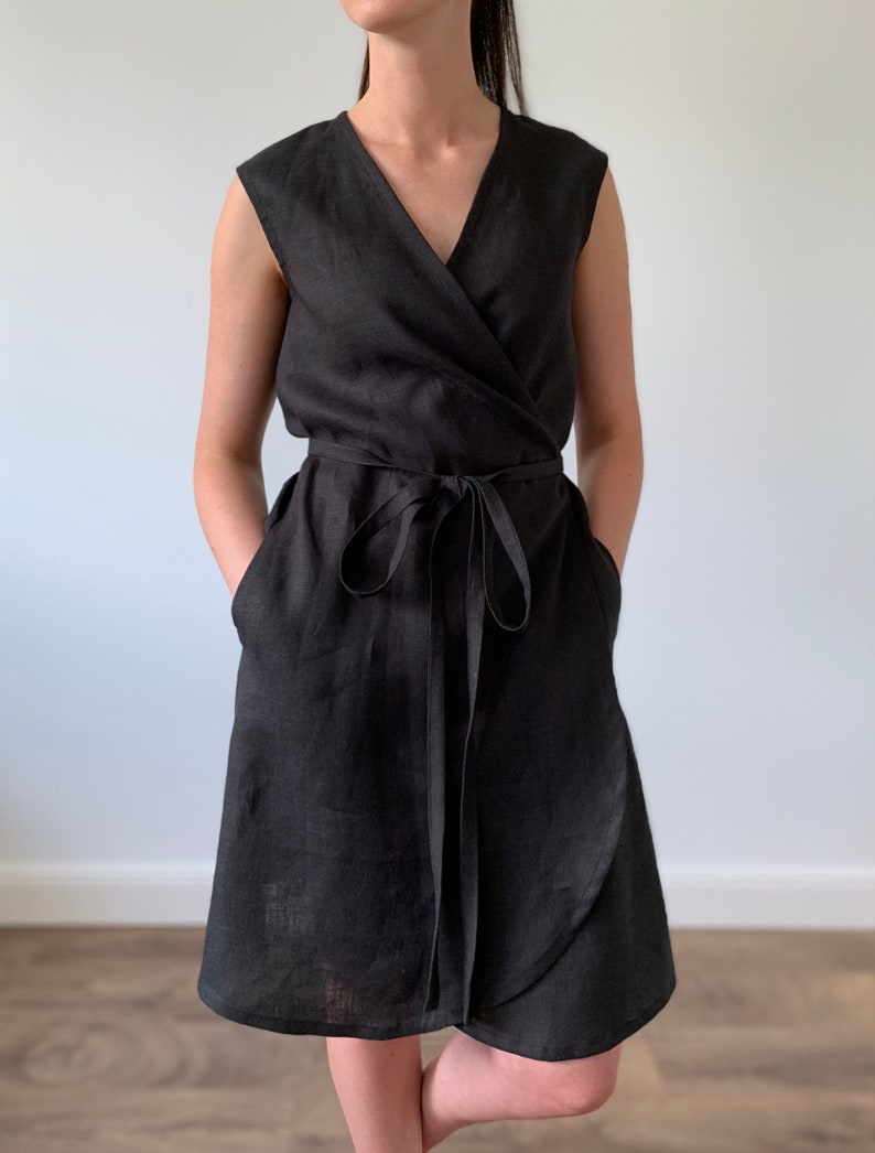May include: A black linen wrap dress with a V-neckline and a tie belt. The dress has pockets on the sides and a slightly flared skirt.