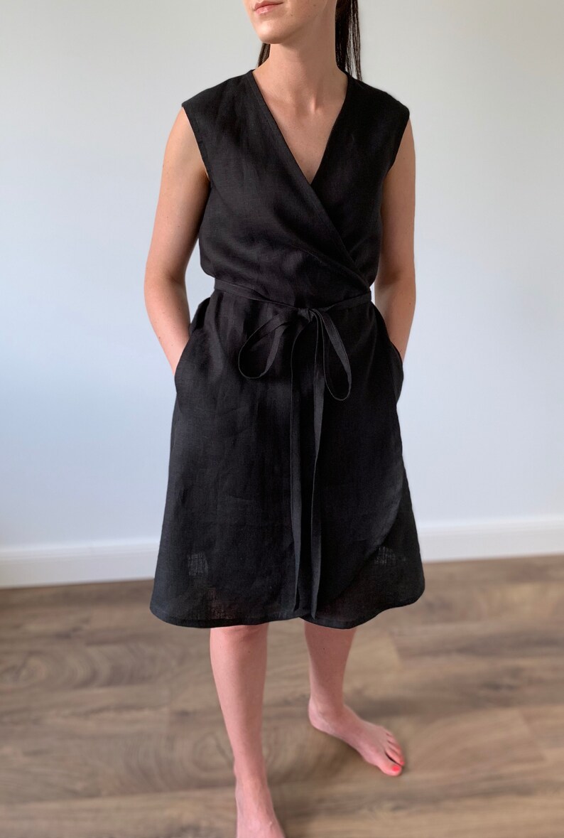 May include: A black linen wrap dress with a V-neckline and short sleeves. The dress has a tie belt at the waist and pockets on the sides.