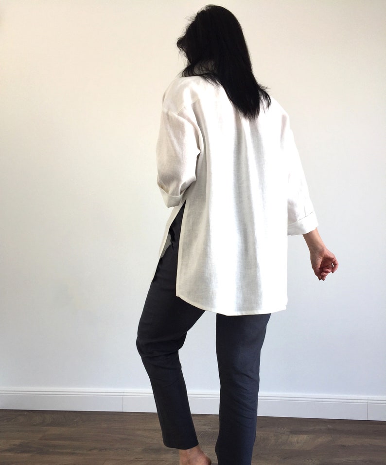 May include: A white linen shirt with long sleeves and a side slit. The shirt is loose fitting and has a relaxed silhouette.