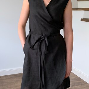 May include: A black linen wrap dress with a V-neckline and short sleeves. The dress has a tie belt at the waist and pockets on the sides.