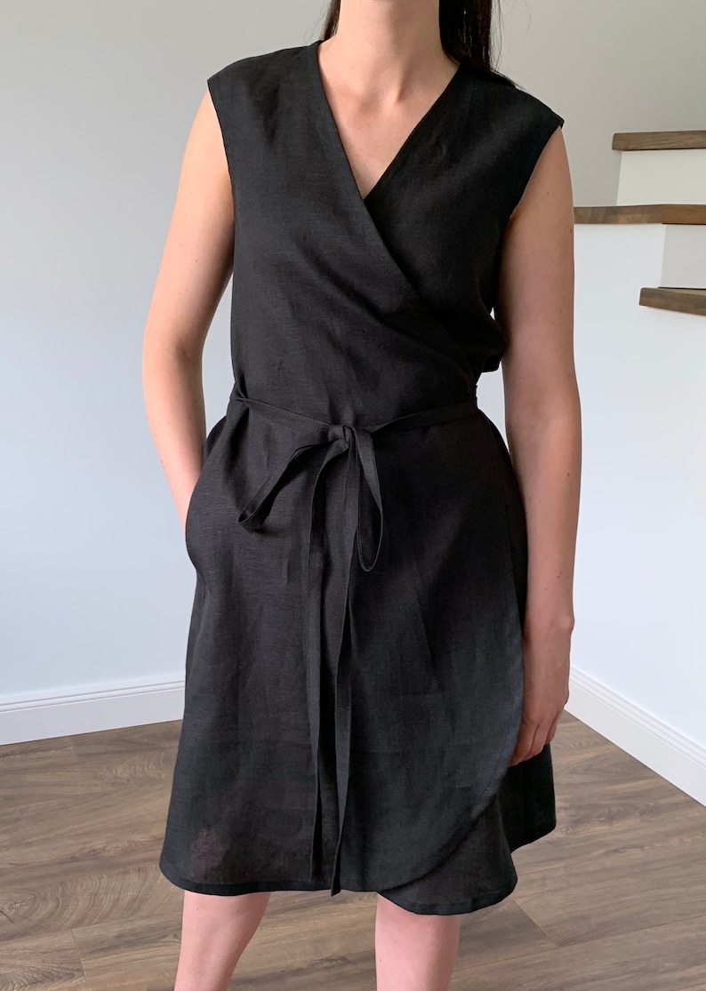 May include: A black linen wrap dress with a V-neckline and short sleeves. The dress has a tie belt at the waist and pockets on the sides.
