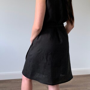 May include: A black sleeveless linen dress with a tie belt. The dress is knee-length and has a relaxed fit.