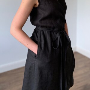May include: A black linen wrap dress with a V-neckline and sleeveless design. The dress has a tie belt and pockets.