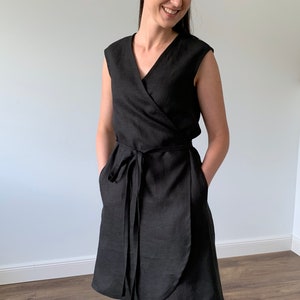 May include: A black linen wrap dress with a V-neckline and short sleeves. The dress has a tie belt and pockets.